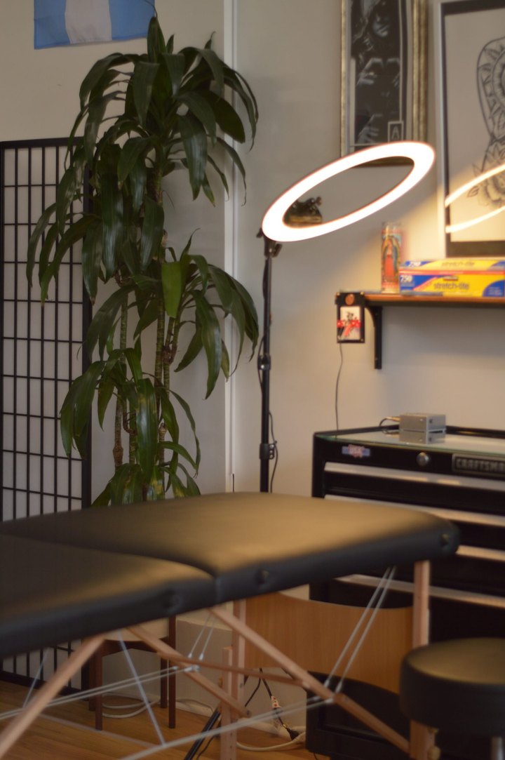An empty tattoo station at La Rosa: black table, shoji screen, tall plant and a ring light.