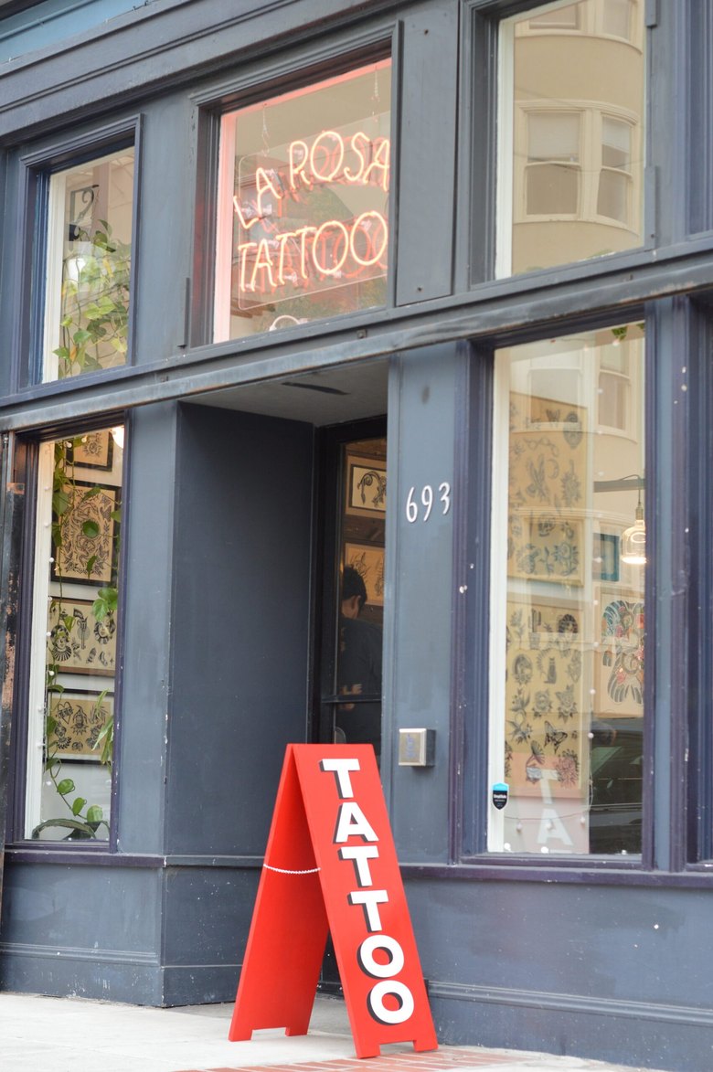 The La Rosa Tattoo storefront at 693 14th St: neon window sign, a red TATTOO a-frame on the sidewalk, flash-lined windows.