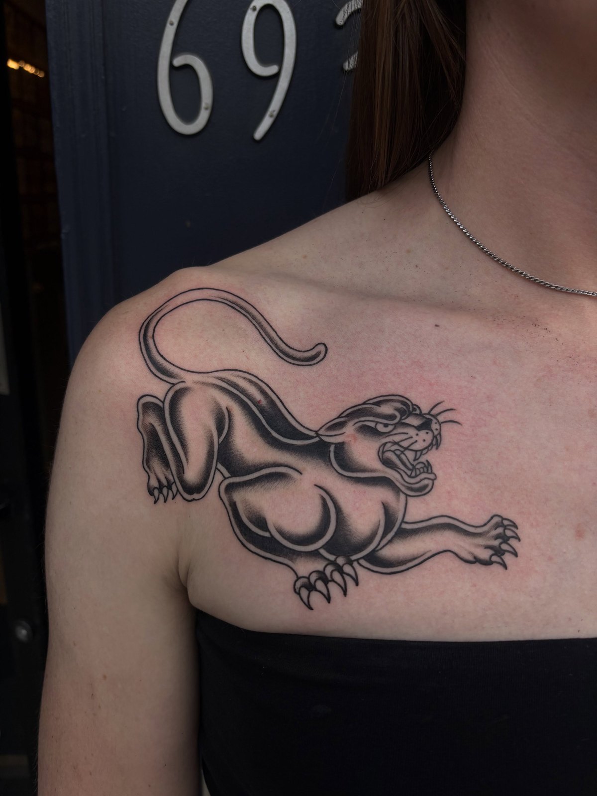 An American traditional crawling panther tattooed across a chest and collarbone, outside the shop's 693 door.