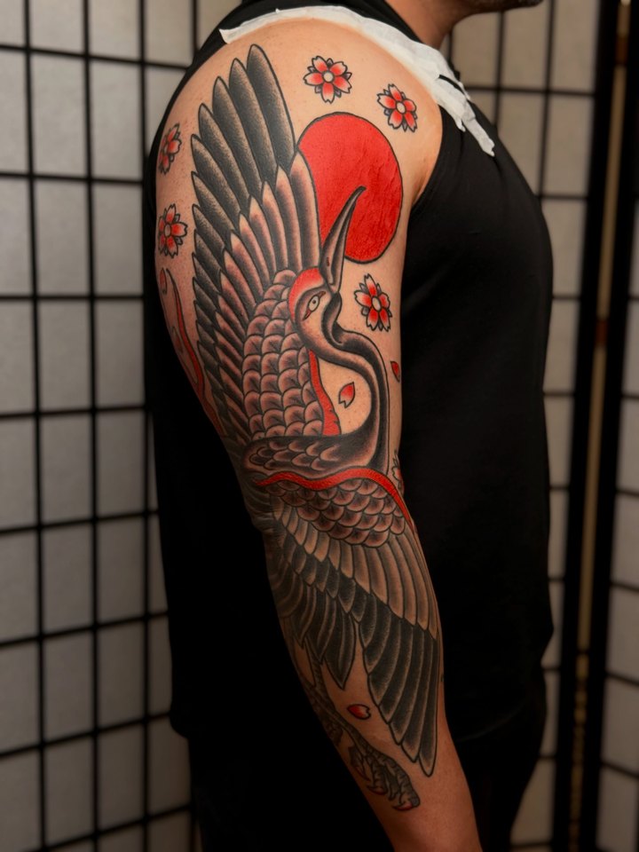 A Japanese irezumi crane with a red rising sun and cherry blossoms covering an upper arm.