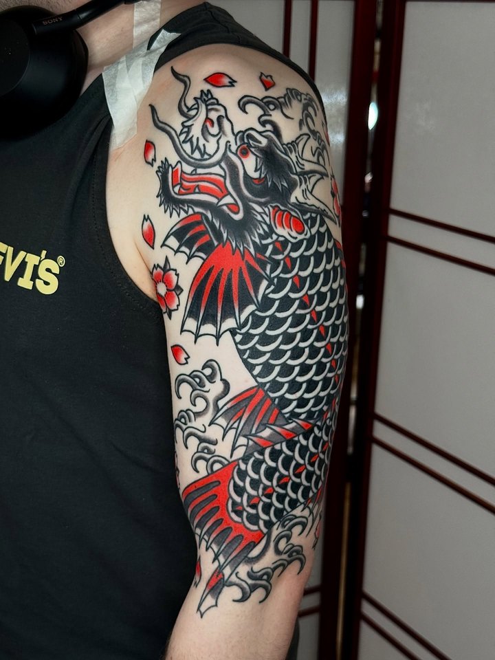A Japanese dragon half sleeve in black, grey and red on an upper arm.