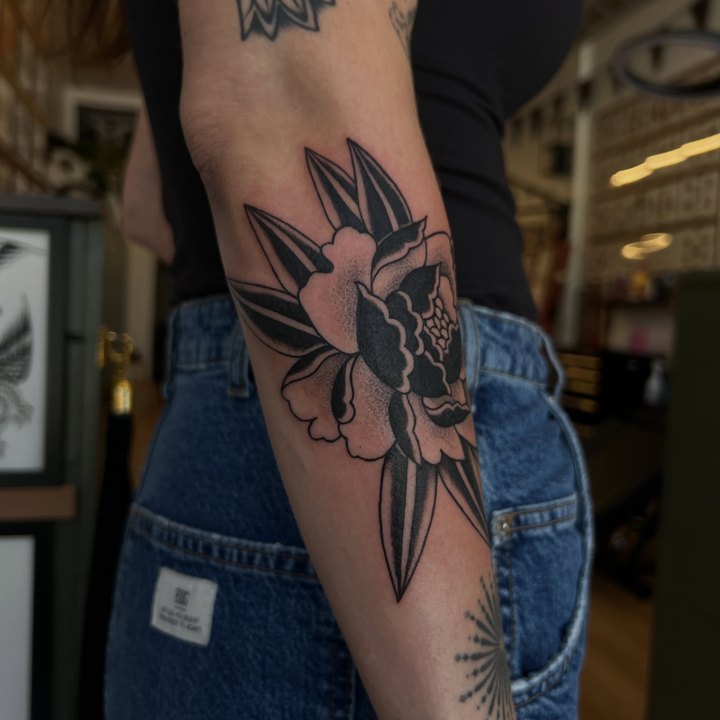 A bold black and grey peony with leaves tattooed on an elbow.
